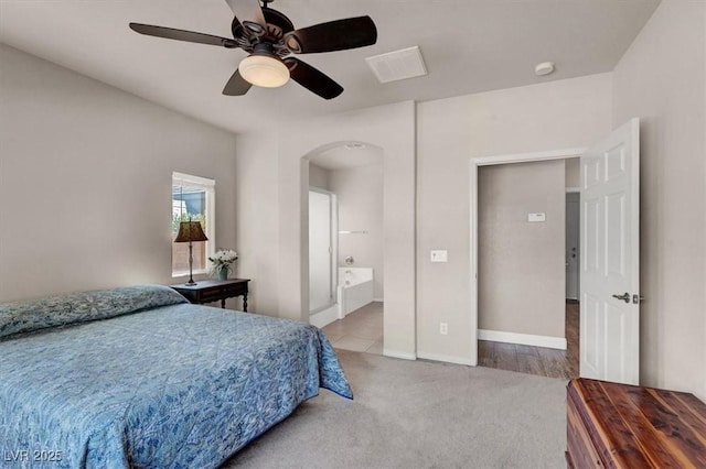 bedroom featuring a ceiling fan, baseboards, arched walkways, carpet flooring, and connected bathroom