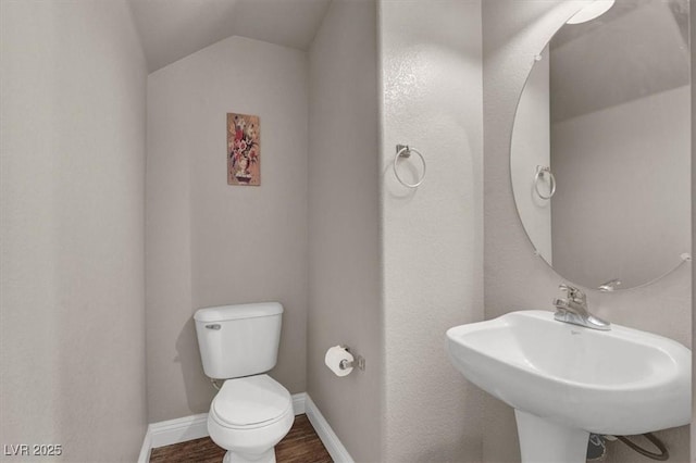 half bathroom featuring toilet, lofted ceiling, a sink, wood finished floors, and baseboards