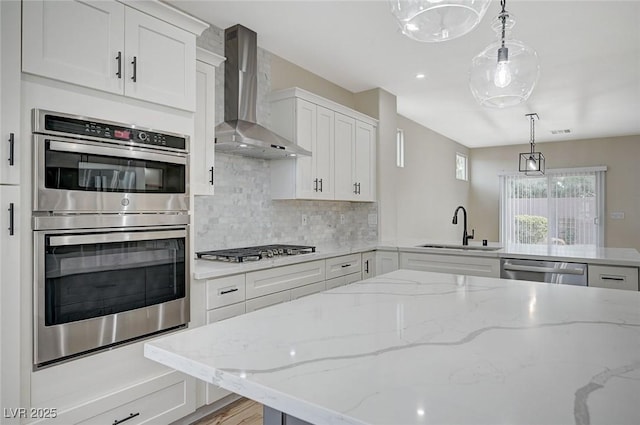 kitchen with a peninsula, a sink, decorative backsplash, appliances with stainless steel finishes, and wall chimney exhaust hood