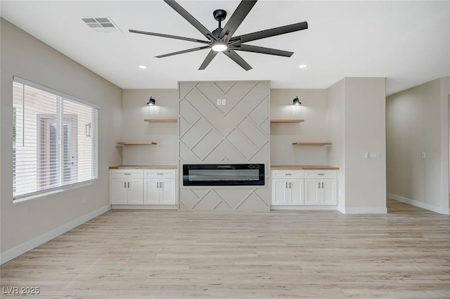 unfurnished living room featuring light wood-type flooring, visible vents, baseboards, and a fireplace