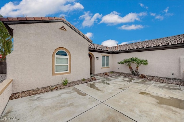 rear view of house with stucco siding, a tile roof, and a patio area