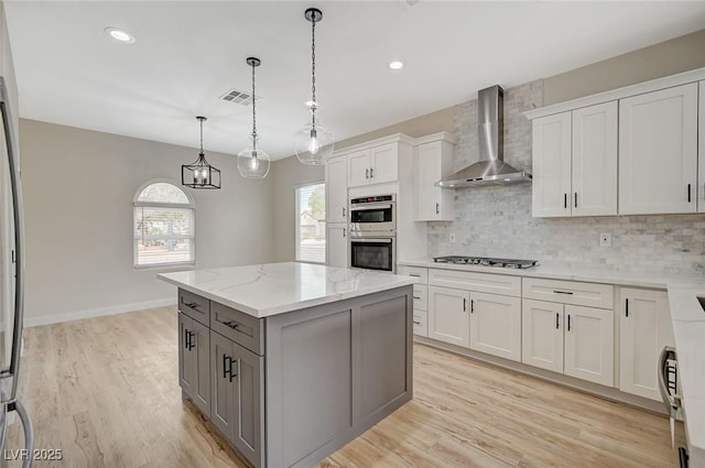 kitchen with tasteful backsplash, a center island, gray cabinets, light wood-style flooring, and wall chimney exhaust hood