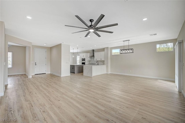 unfurnished living room featuring a healthy amount of sunlight, a ceiling fan, visible vents, and light wood-type flooring