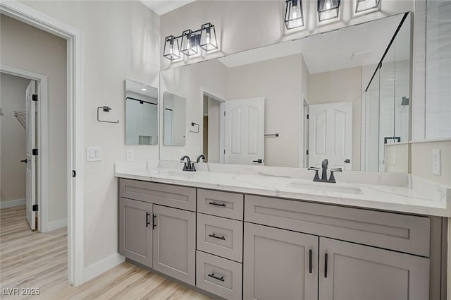 bathroom featuring a shower stall, wood finished floors, double vanity, and a sink