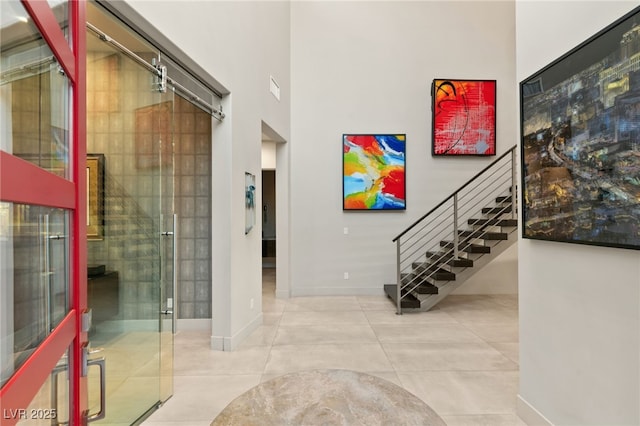 entryway with tile patterned floors, stairway, baseboards, and a towering ceiling