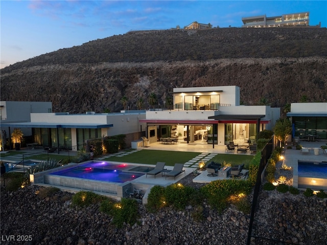 515 Serenity Point Dr, Henderson, NV 89012 - back of property at dusk featuring a patio, a mountain view, outdoor lounge area, a pool with connected hot tub, and stucco siding