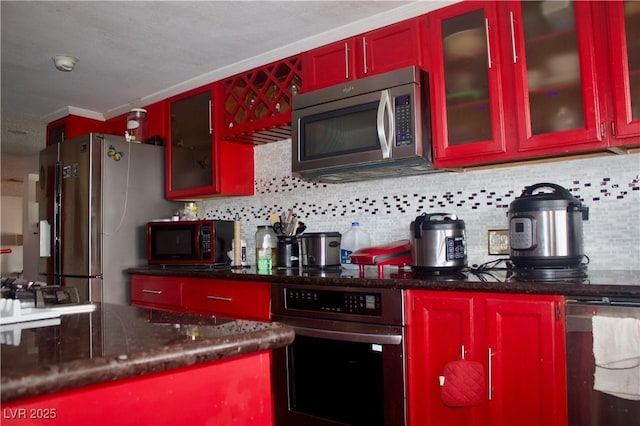 kitchen with backsplash, stainless steel appliances, dark stone counters, crown molding, and glass insert cabinets