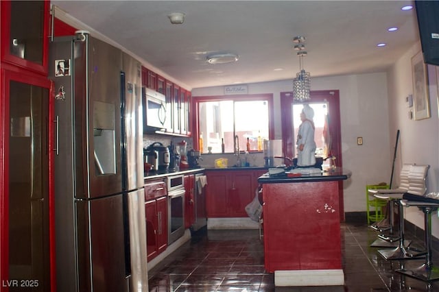 kitchen with a sink, dark tile patterned flooring, appliances with stainless steel finishes, hanging light fixtures, and reddish brown cabinets