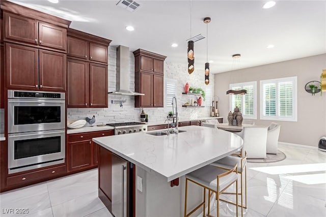 kitchen featuring visible vents, a sink, appliances with stainless steel finishes, pendant lighting, and wall chimney exhaust hood