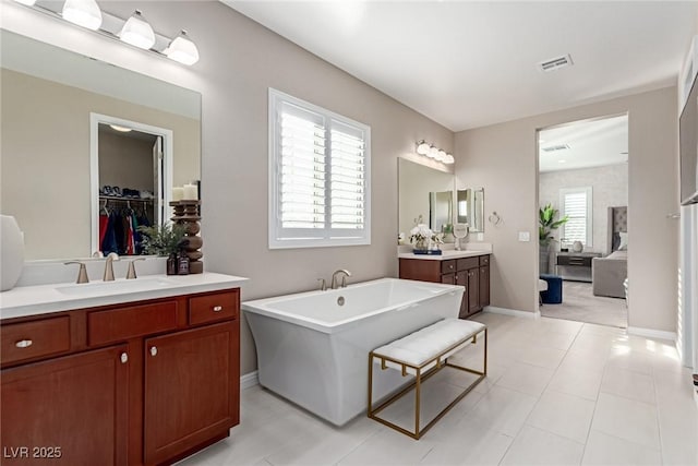 bathroom featuring visible vents, two vanities, a sink, baseboards, and a freestanding bath