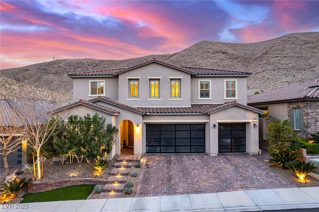 view of front of home featuring stucco siding, decorative driveway, a mountain view, a garage, and a tiled roof