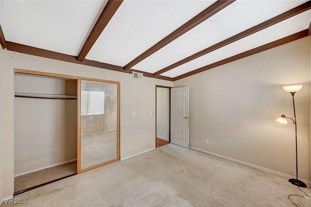 unfurnished bedroom featuring visible vents, a textured ceiling, a closet, carpet flooring, and vaulted ceiling with beams