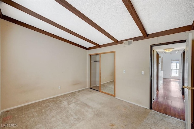 unfurnished bedroom featuring baseboards, visible vents, lofted ceiling with beams, a textured ceiling, and light colored carpet