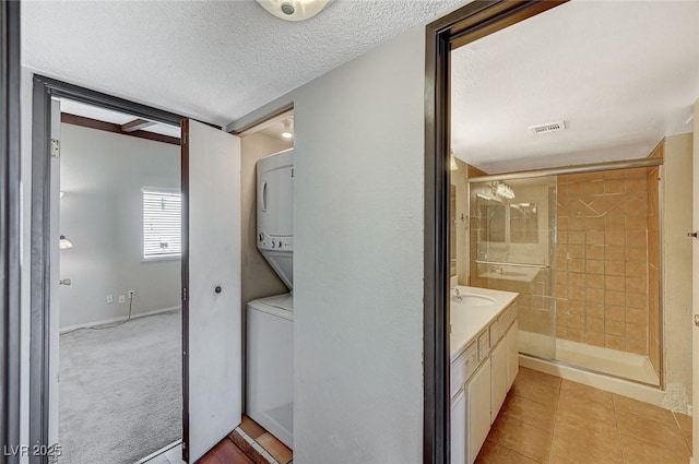 bathroom with vanity, visible vents, stacked washing maching and dryer, a stall shower, and a textured ceiling