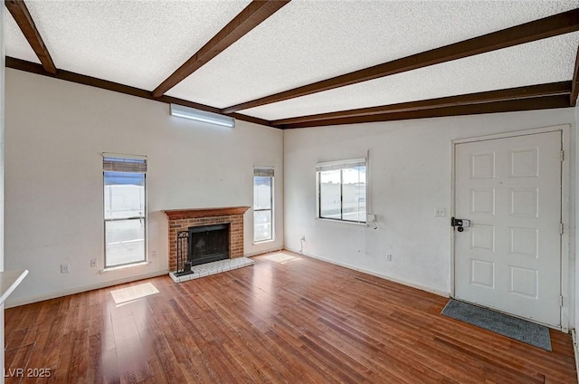 unfurnished living room with baseboards, beamed ceiling, a fireplace, wood finished floors, and a textured ceiling