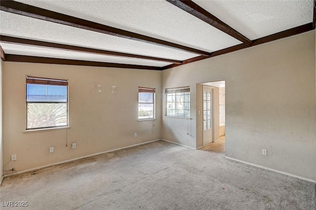 empty room with light colored carpet, beam ceiling, a textured ceiling, and baseboards