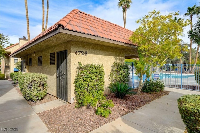 view of home's exterior featuring stucco siding, a community pool, fence, and a tiled roof