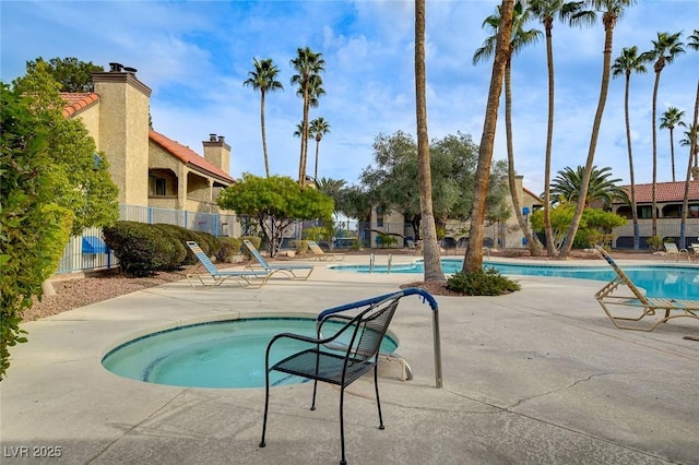 pool with a patio area, a community hot tub, and fence