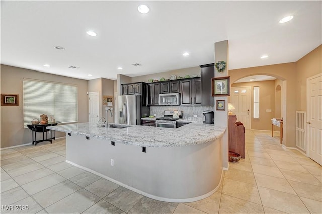 kitchen featuring a sink, stainless steel appliances, arched walkways, light tile patterned floors, and light stone countertops