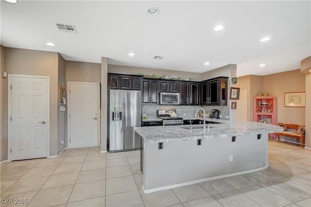 kitchen with tasteful backsplash, light stone countertops, a breakfast bar, stainless steel appliances, and a sink