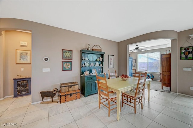 dining area featuring arched walkways, light tile patterned floors, a ceiling fan, and baseboards