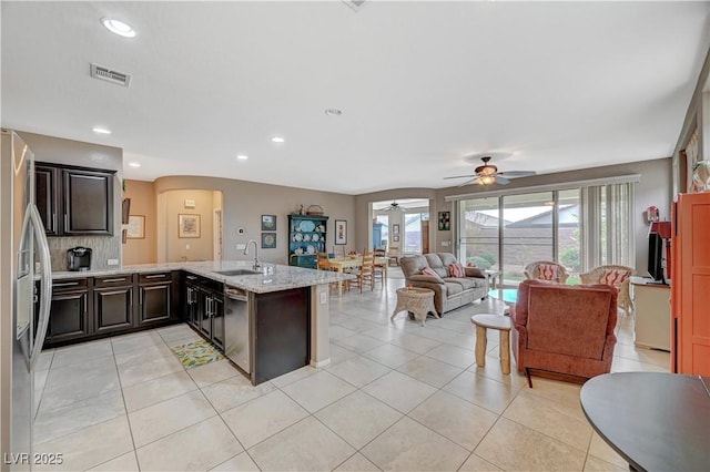 kitchen with light stone countertops, a peninsula, light tile patterned flooring, a sink, and stainless steel appliances