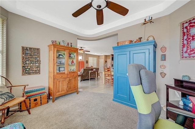 living area with ceiling fan, a tray ceiling, and light carpet