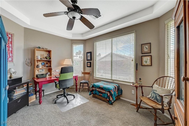 carpeted office space featuring ceiling fan, baseboards, and a tray ceiling