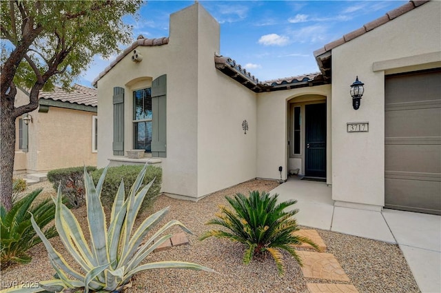 entrance to property featuring stucco siding, a tiled roof, and an attached garage