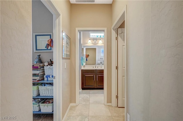 hall with light tile patterned flooring, visible vents, baseboards, and a sink