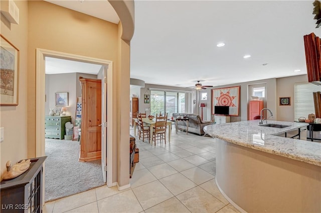 kitchen featuring light stone countertops, light colored carpet, light tile patterned floors, recessed lighting, and a sink