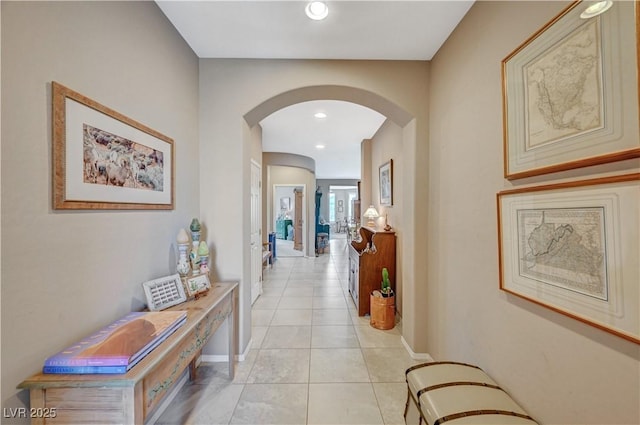 corridor with light tile patterned floors, baseboards, arched walkways, and recessed lighting