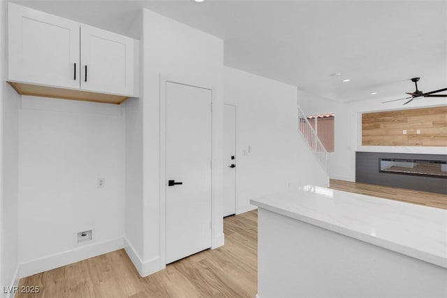 kitchen with light wood-type flooring, a glass covered fireplace, white cabinetry, light stone countertops, and ceiling fan