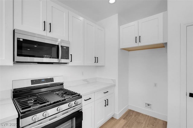 kitchen with baseboards, appliances with stainless steel finishes, white cabinetry, and light wood-style floors