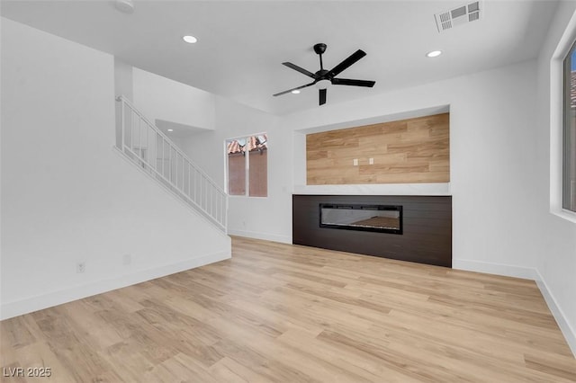 unfurnished living room featuring visible vents, wood finished floors, baseboards, and a glass covered fireplace