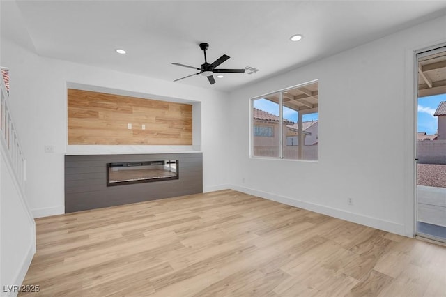 unfurnished living room with recessed lighting, wood finished floors, a healthy amount of sunlight, and a glass covered fireplace