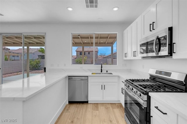 kitchen with visible vents, light stone countertops, appliances with stainless steel finishes, white cabinetry, and a sink