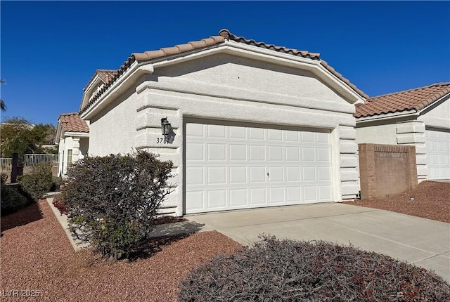 view of home's exterior with fence, a tiled roof, concrete driveway, stucco siding, and an attached garage