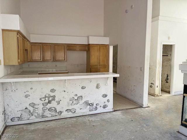 kitchen featuring tile countertops, concrete floors, a peninsula, brown cabinetry, and a towering ceiling