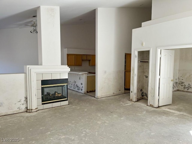 unfurnished living room with a ceiling fan, unfinished concrete floors, a towering ceiling, and a tiled fireplace