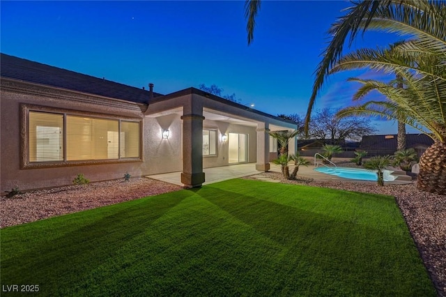 rear view of property with a patio area, a yard, a fenced in pool, and stucco siding