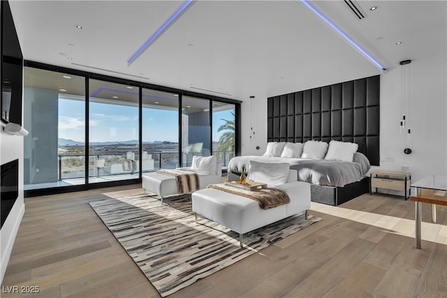 bedroom with a wall of windows, wood finished floors, access to exterior, and a fireplace