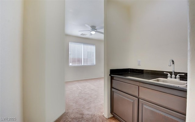 kitchen with dark countertops, visible vents, ceiling fan, light colored carpet, and a sink