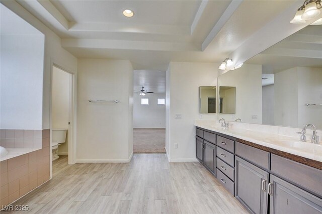 bathroom with toilet, a tray ceiling, double vanity, wood finished floors, and a sink