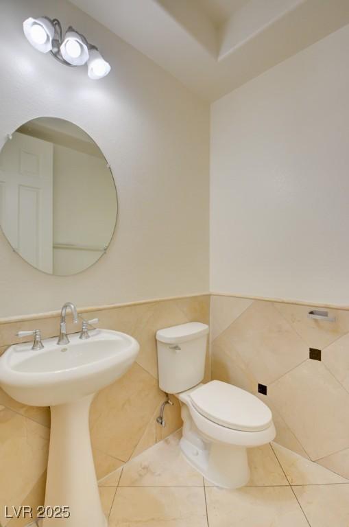 half bathroom featuring tile patterned flooring, tile walls, toilet, and wainscoting