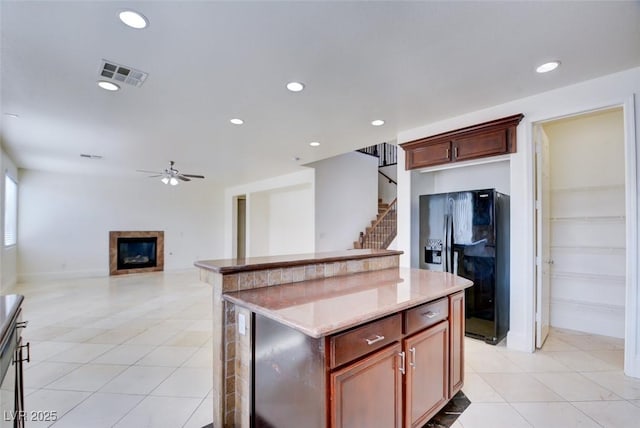 kitchen with a glass covered fireplace, light tile patterned flooring, visible vents, and black refrigerator with ice dispenser