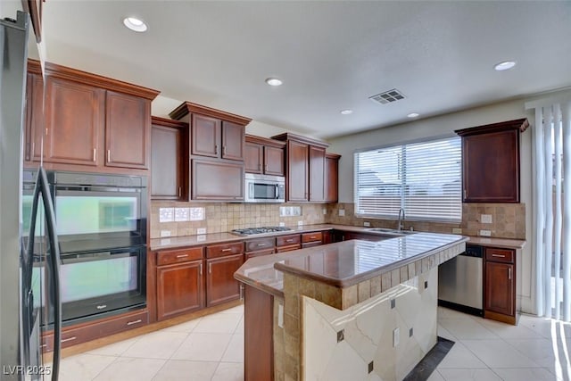 kitchen with light tile patterned floors, visible vents, a kitchen island, stainless steel appliances, and backsplash