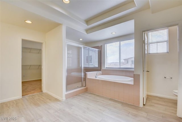 bathroom featuring a shower stall, a walk in closet, toilet, wood finished floors, and a bath