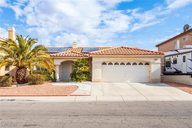 mediterranean / spanish-style house with a tiled roof, roof mounted solar panels, stucco siding, driveway, and an attached garage