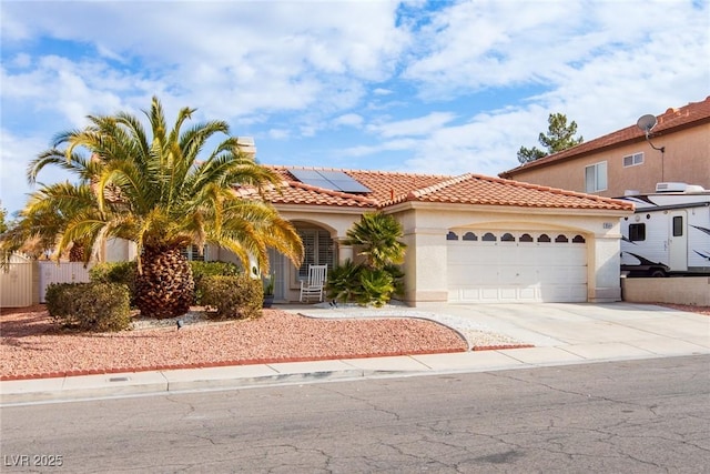 mediterranean / spanish-style home with an attached garage, a tiled roof, roof mounted solar panels, stucco siding, and driveway